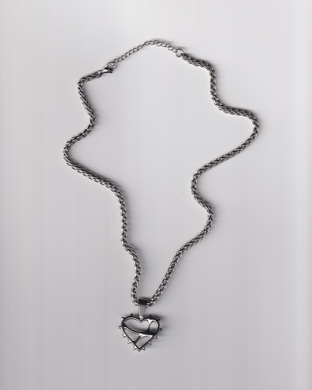 Silver necklace with a heart-shaped pendant on a light gray background